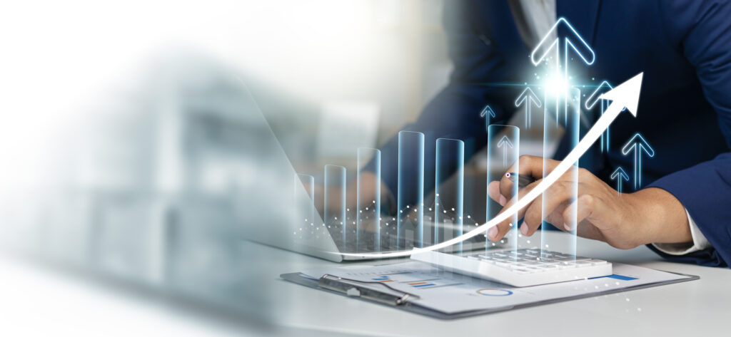 Someone witting by a computer and with a calculator. Digitallly illustrated arrows pointing up on top if the image.